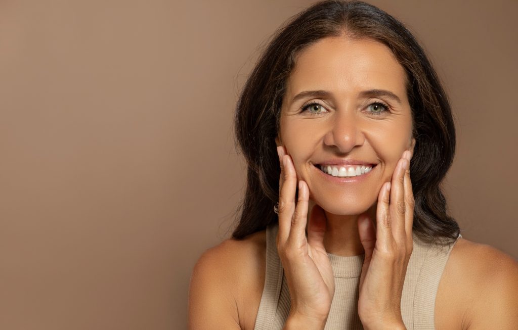Happy caucasian elderly woman touching face with hands, enjoy anti-wrinkle treatment, natural beauty